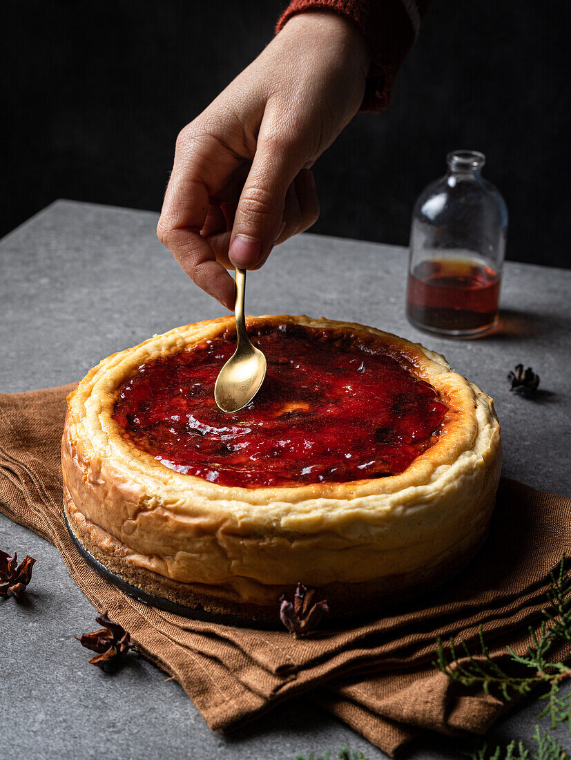 Crop unrecognizable chef spreading sweet jam on cooked homemade cheesecake served on gray table with fir tree