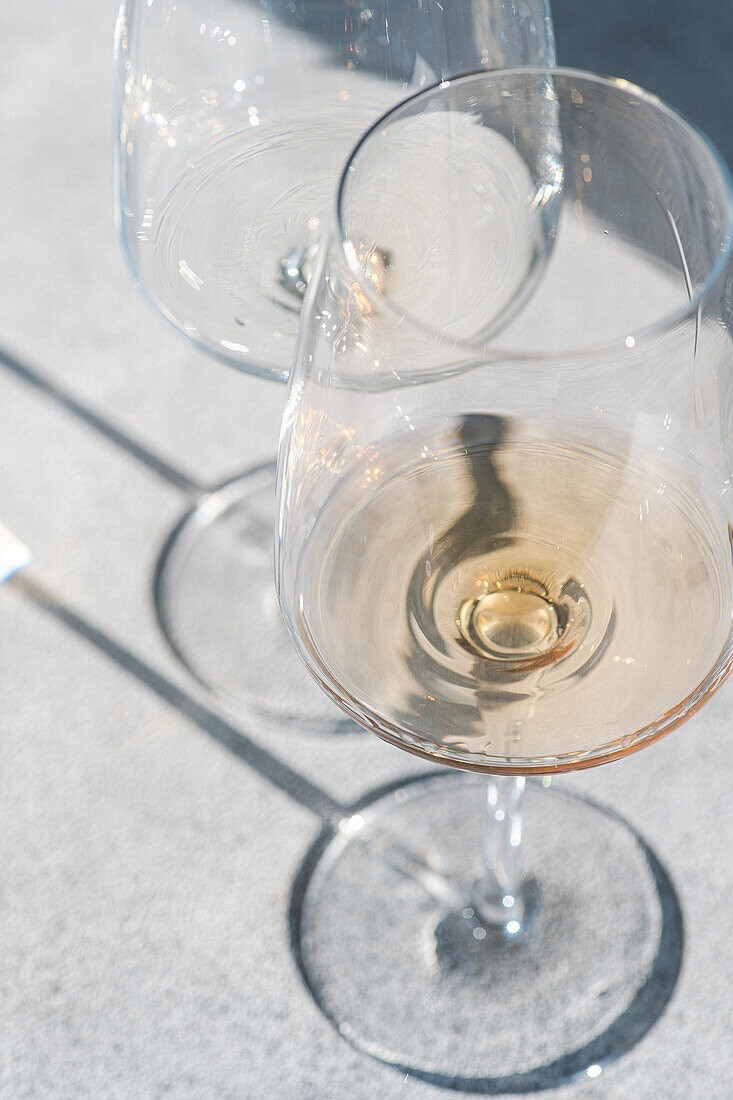 Ein Paar Weingläser mit verschiedenen Arten von trockenem Weißwein auf grauem Betonhintergrund mit tiefen Schatten