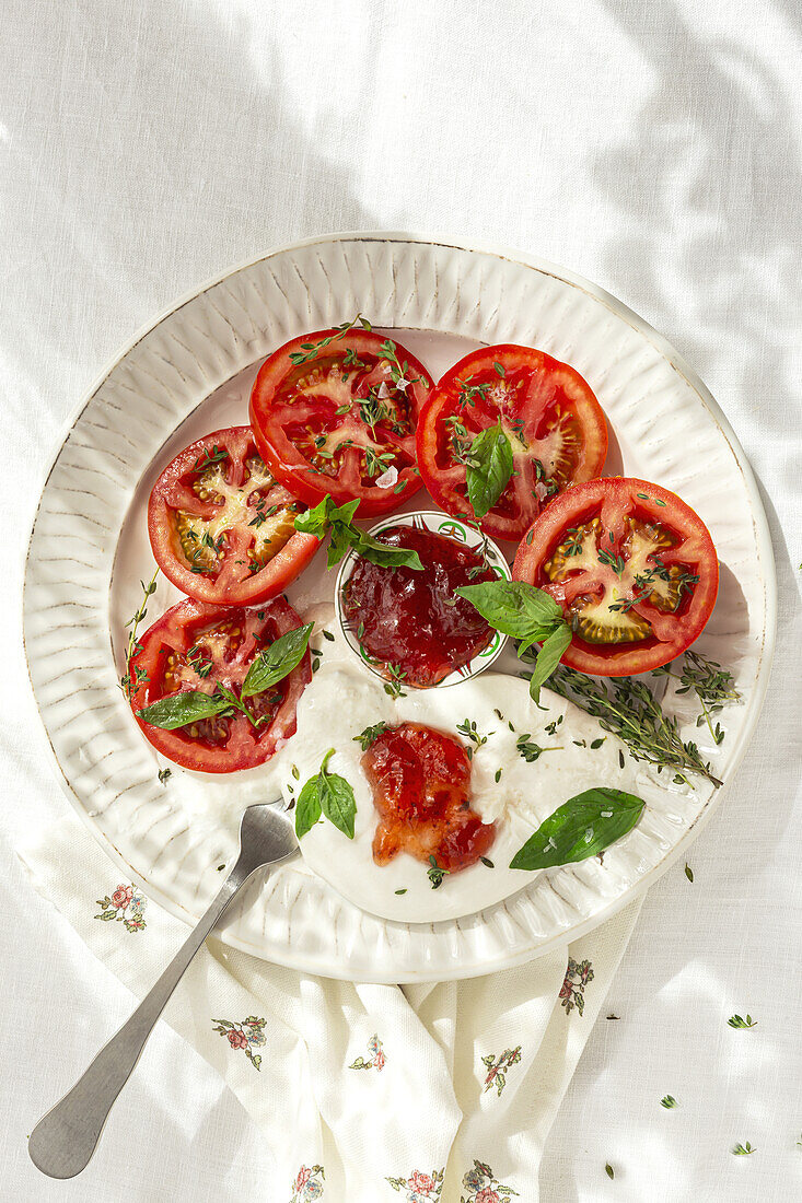 Top view of slices of fresh tomato and mozzarella cheese with sauce and herbs served on plate on table in daylight