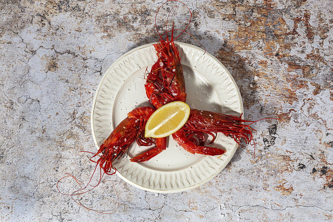 Tasty seafood of cooked red shrimps with fresh lemon slices and coarse salt on white background