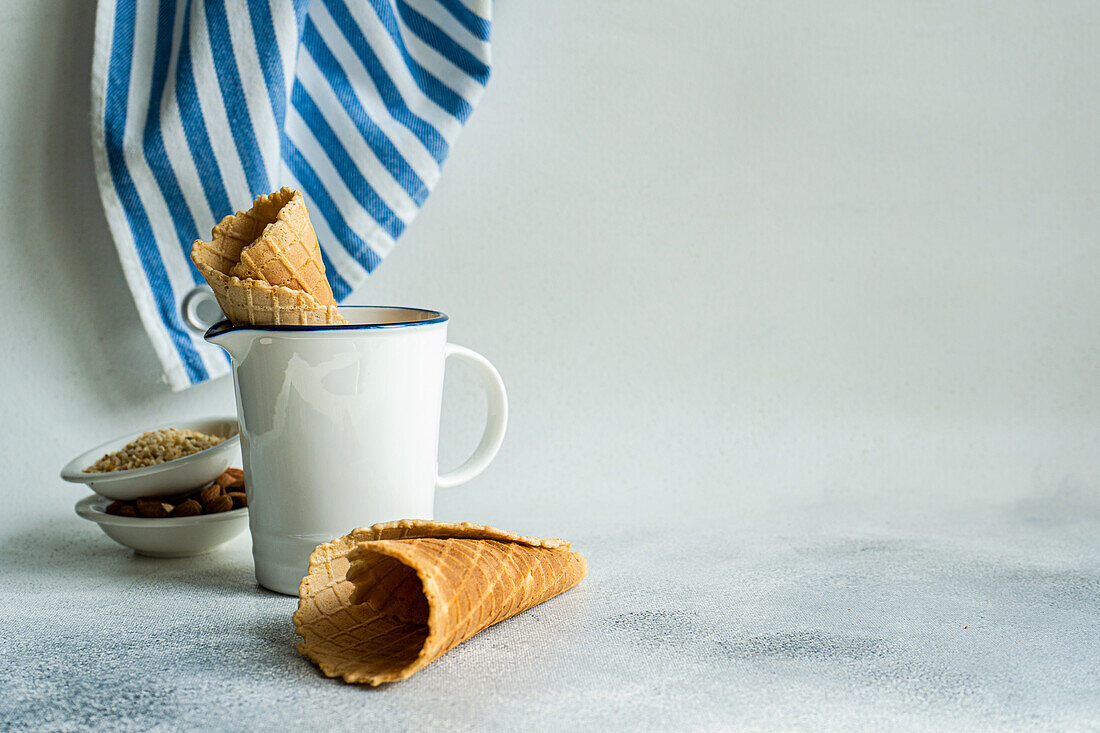 Waffle cones and nuts for ice cream preparation on concrete table with white concrete background with towel