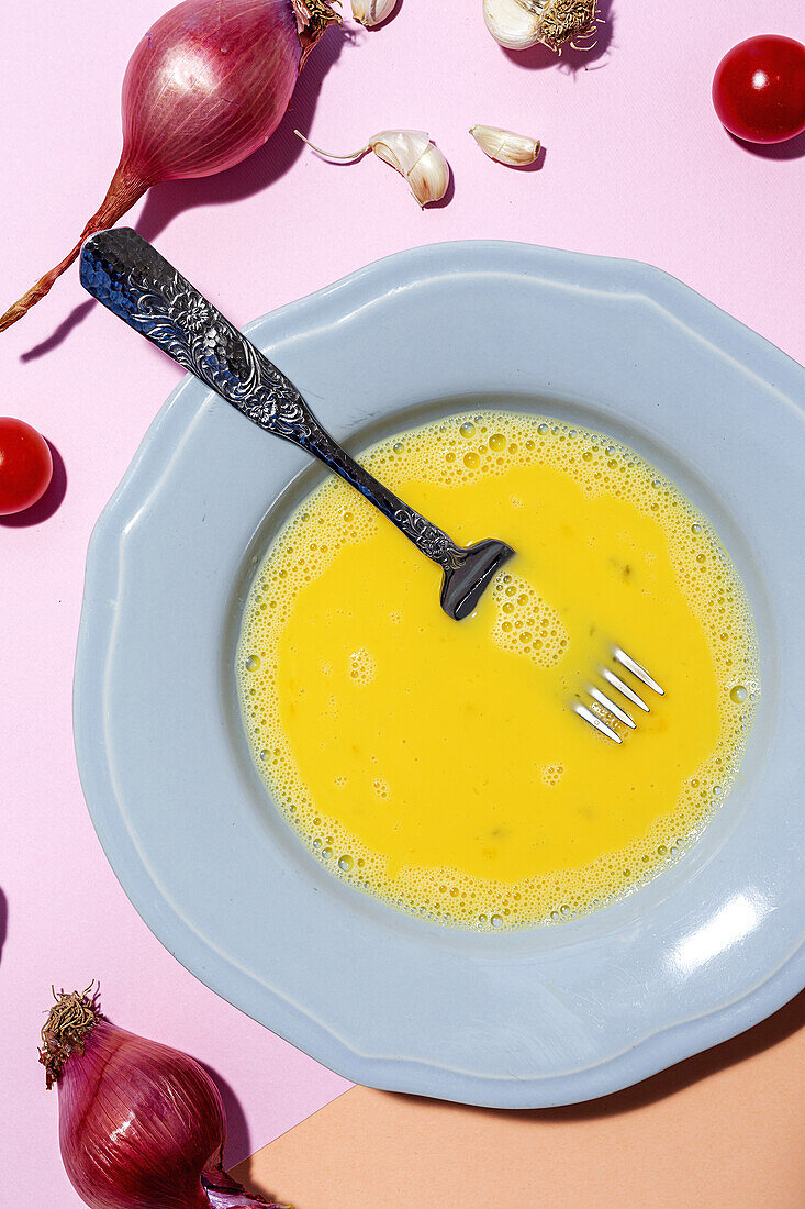 Overhead view beaten egg on the plate against ripe red onions