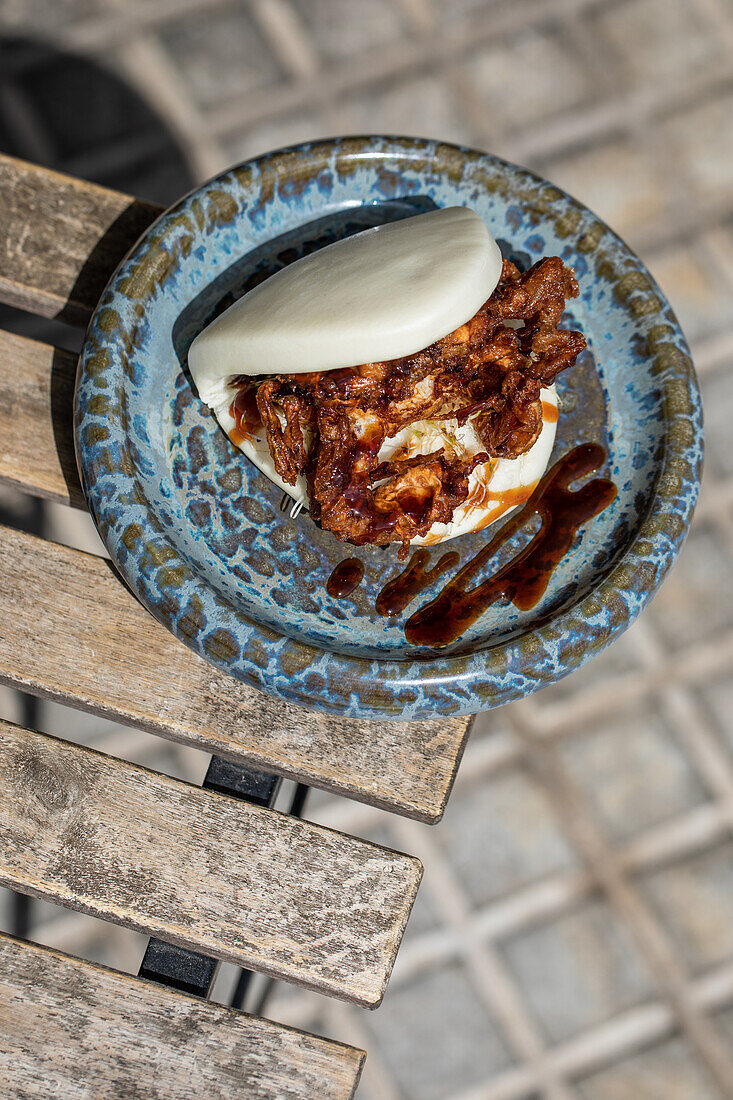 Köstliches japanisches Pan Bao Brötchen mit gebratenen Weichschalenkrabben, serviert auf einer Tischecke auf der Terrasse eines Restaurants (von oben)