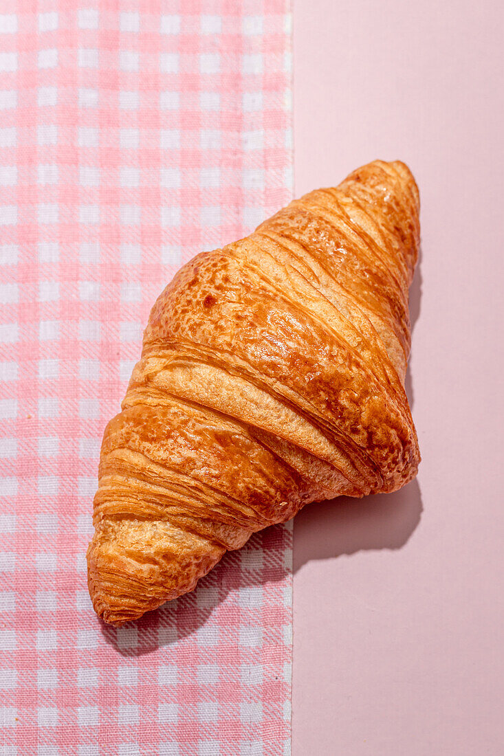 From above of delicious sweet croissant placed on pink tablecloth on table in daylight