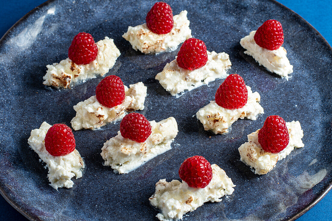 Top view of appetizing homemade dessert with cream and raspberries on plate placed on blue background