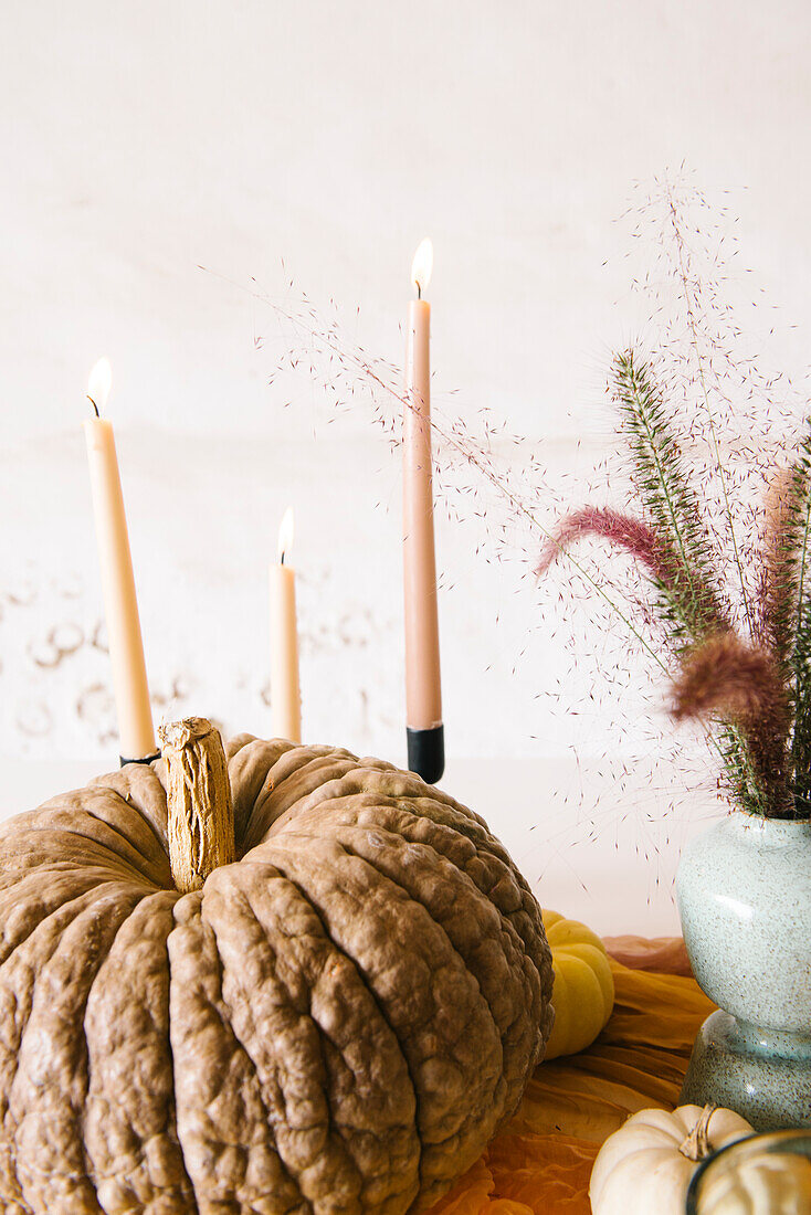 Kreative Tischdekoration mit verschiedenen Kürbissen, brennenden Kerzen und Vasen mit trockenen Pflanzen in der Nähe von Keramiktellern und Gläsern während eines Halloween-Dinners