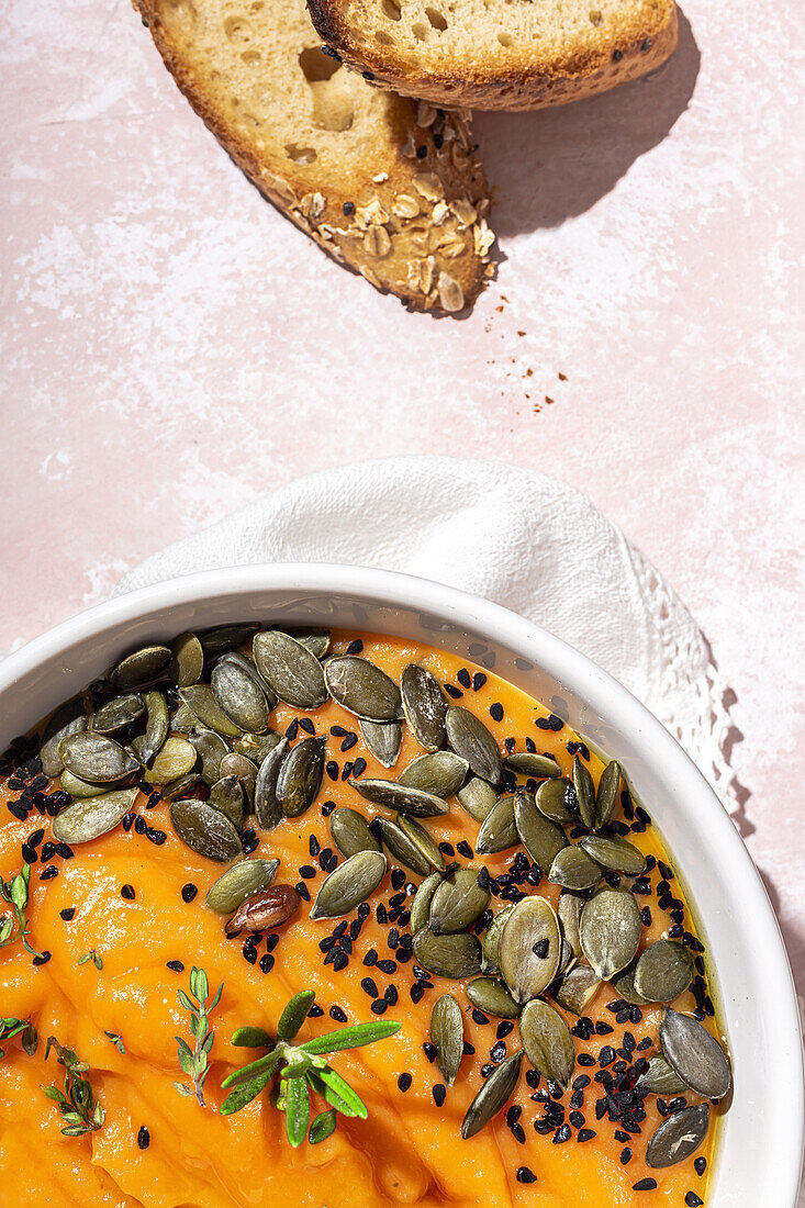 Top view of appetizing homemade pumpkin puree with seeds and herbs in bowl placed on table near crispy bread slices in kitchen