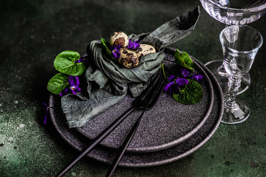 Frühlingshaft gedeckter Tisch mit blauer Viola-Blüte auf schwarzem Tellerset
