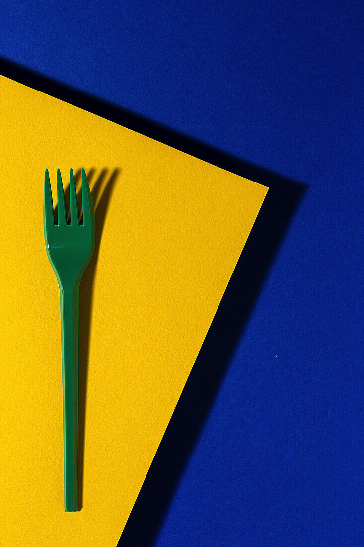 Overhead view of bright green eco friendly fork near yellow carton sheet on blue background