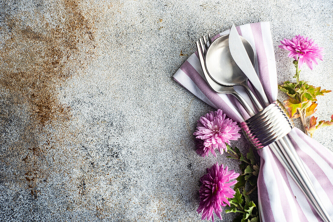 Place setting with cutlery and autumnal purple Chrysanthemum flowers on stripped napkin