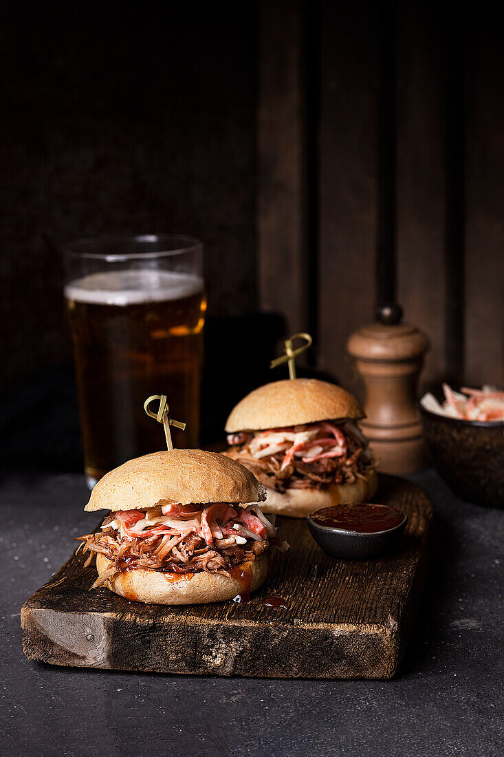 Delicious hamburgers with pulled pork and coleslaw salad in crispy buns served on rustic wooden board
