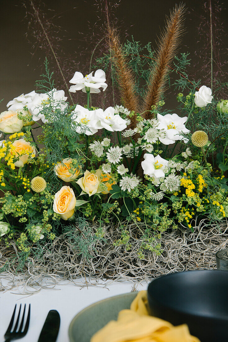 From above of plate and bowl with cutlery and napkin served on table decorated with gentle fresh white and yellow flowers