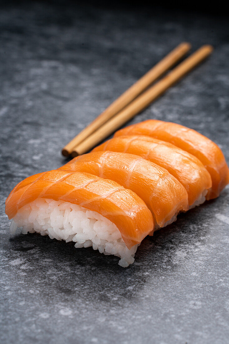 Set of similar tasty traditional Japanese sushi with white rice and fresh salmon served on marble table near wooden chopsticks in light room