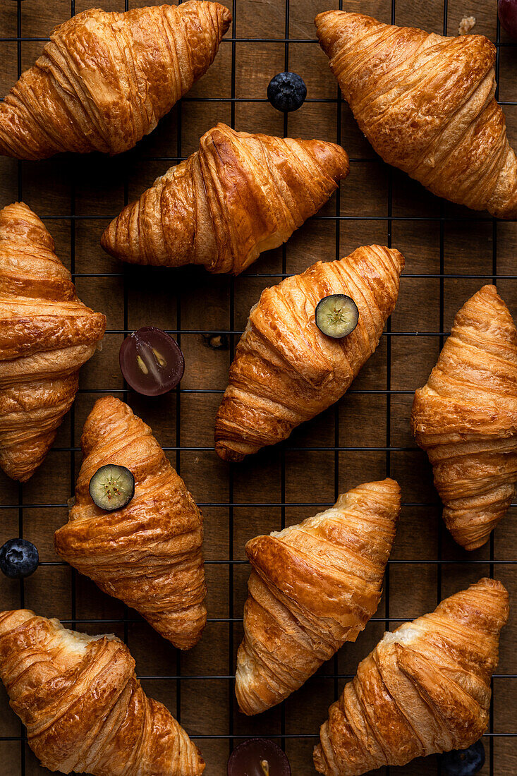 Blick von oben auf leckere süße, frisch gebackene Croissants mit Früchten auf einem Metallgitter auf einem Holztisch