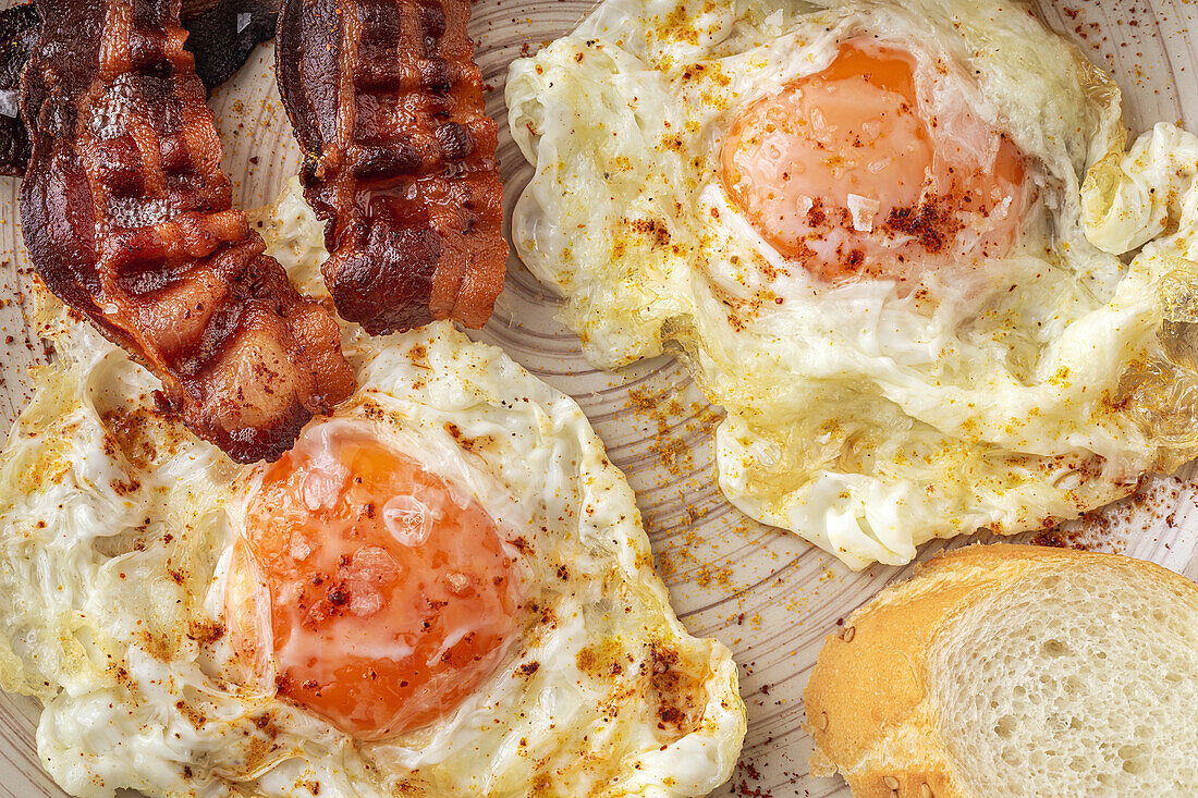 Tasty sunny side up eggs with fried bacon strips on plate