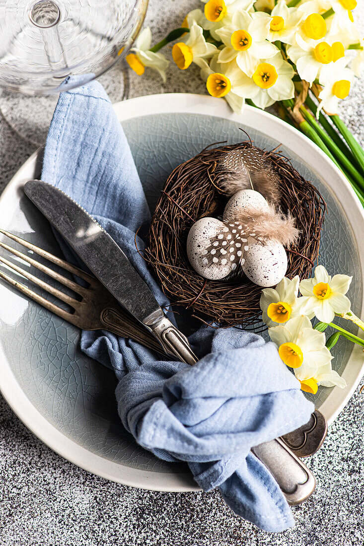 From above easter dinner table set with eggs in the nest and daffodil flowers on concrete background