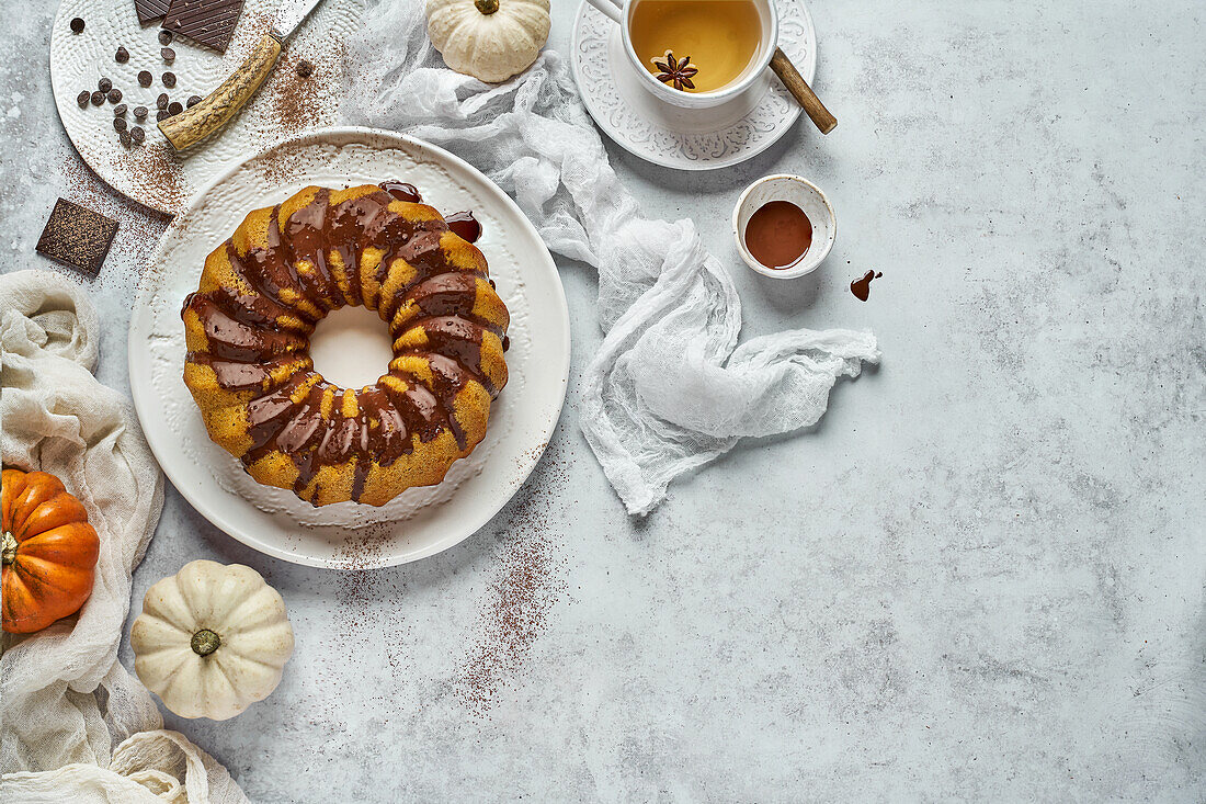 From above autumn breakfast composition with homemade round cruller with chocolate topping cup of warm drink and little pumpkins on white background