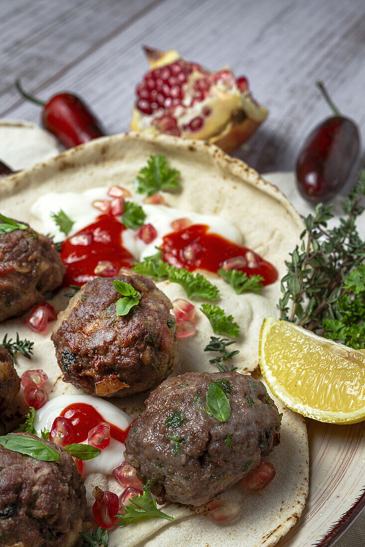 Traditional homemade beef and lamb meatballs with arabic bread, tomato sauce, pomegranate and aromatic herbs. Halal food