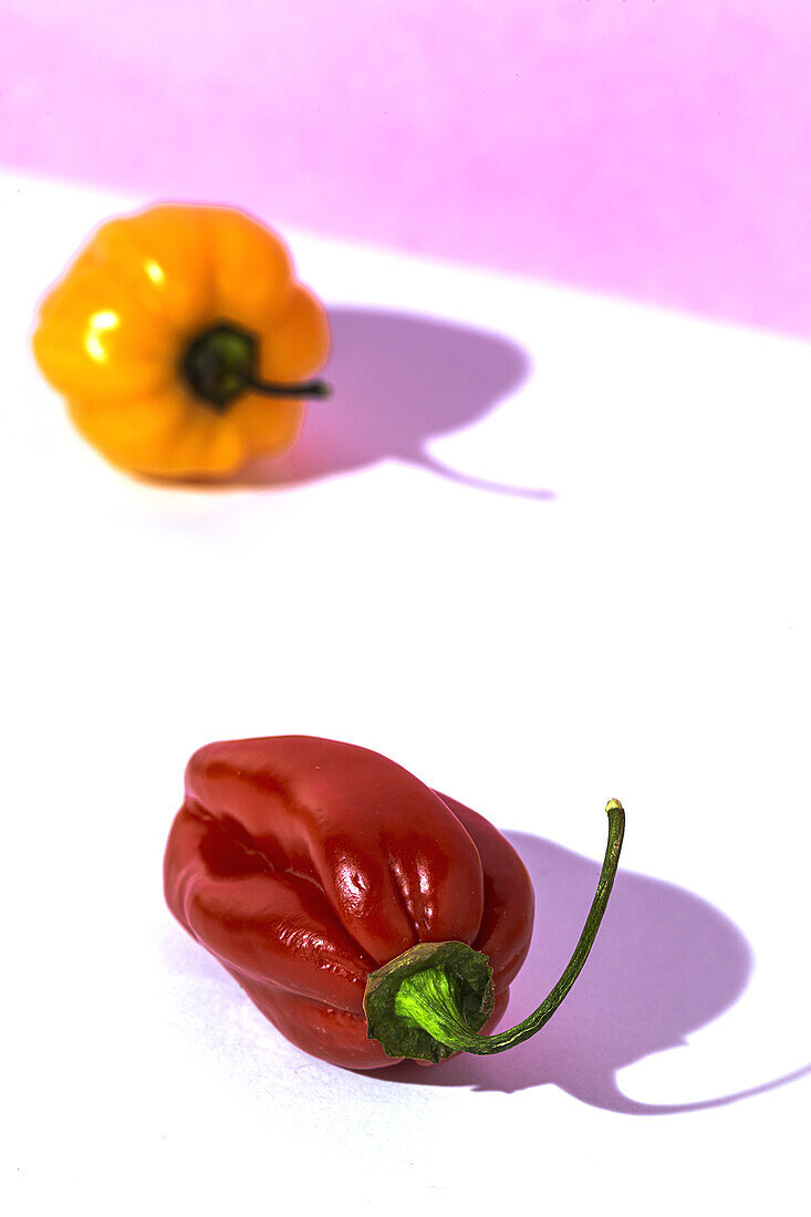 From above of one ripe yellow pepper placed among many red peppers on white table in studio