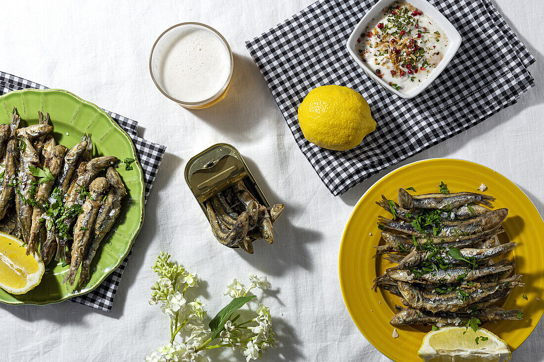 From above of traditional Spanish fried boquerones served on plates with lemons and bowl of white gazpacho soup placed on table with glass of beer in restaurant