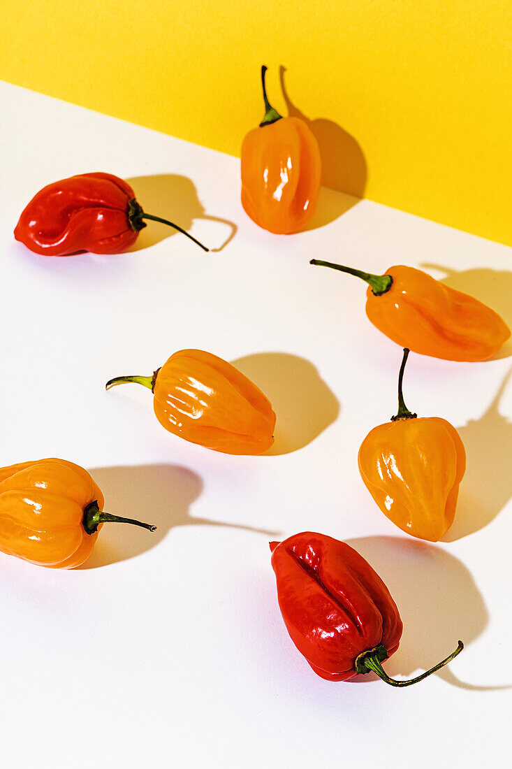 From above of one ripe yellow pepper placed among many red peppers on white table in studio