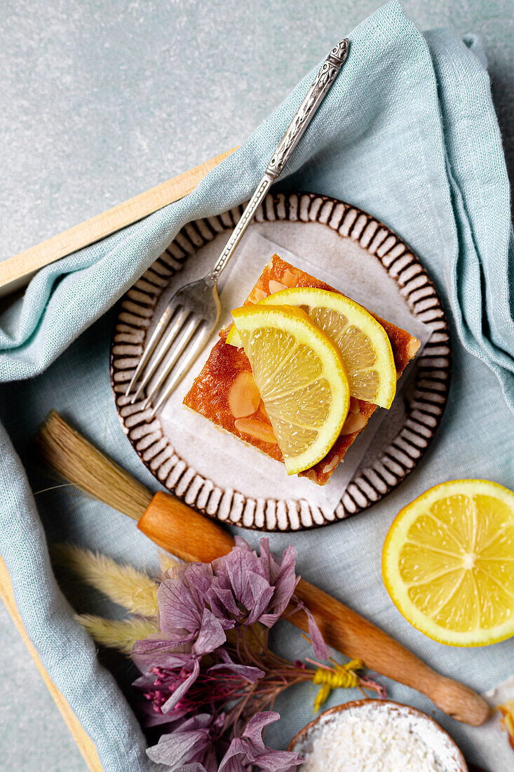 Top view of square slice of delicious homemade lemon cake served on plate with fork on tray with decorative flower