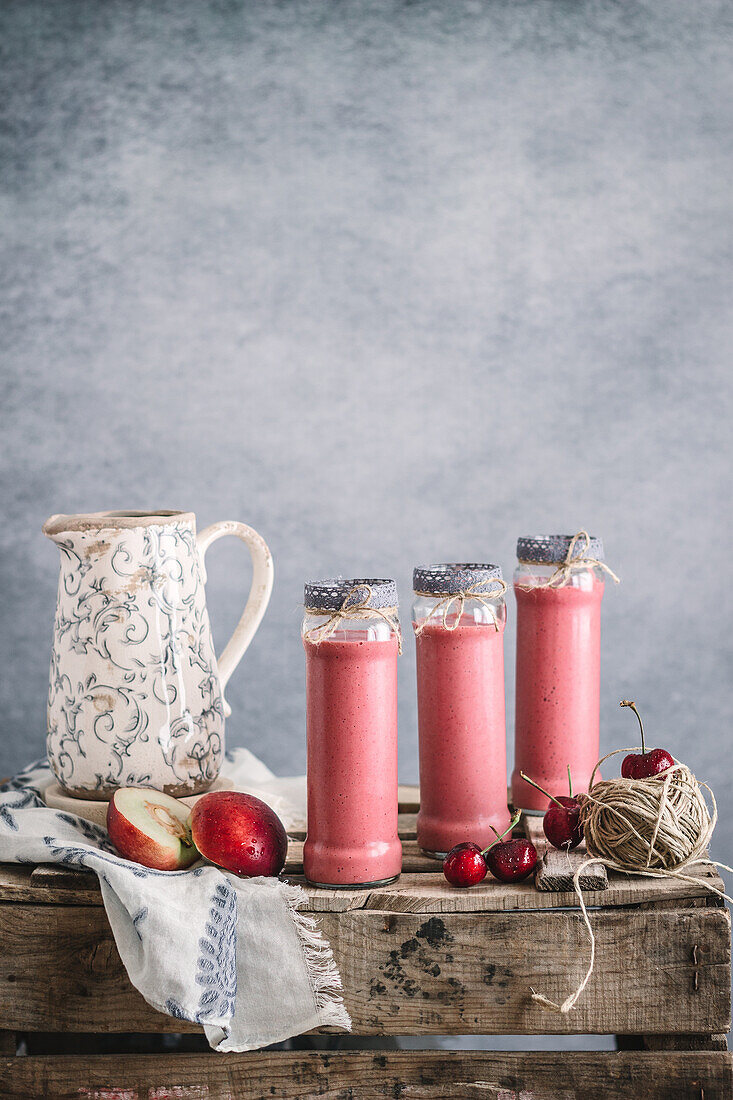 Erfrischender Milchshake mit Nektarinen und Kirsche, serviert in Gläsern auf einem Holztisch mit Blumen