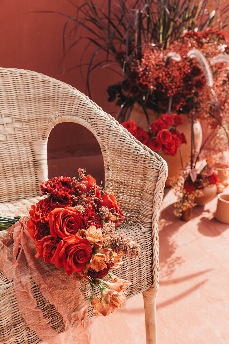 Frische rote Blumen in einem mit dünnem Band gebundenen Strauß auf einem Korbsessel bei Sonnenschein