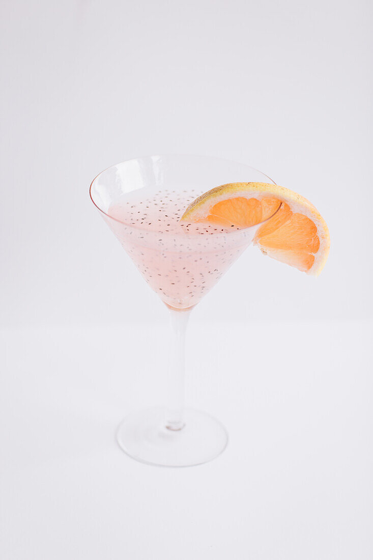 Von oben auf ein Glas mit frischem rosa Martini-Cocktail mit Chia-Samen, garniert mit einer Scheibe Grapefruit, auf weißem Hintergrund