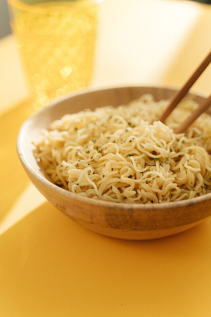 From above bowl of delicious noodles with seasoning placed on yellow background with wooden chopsticks and glass in light room