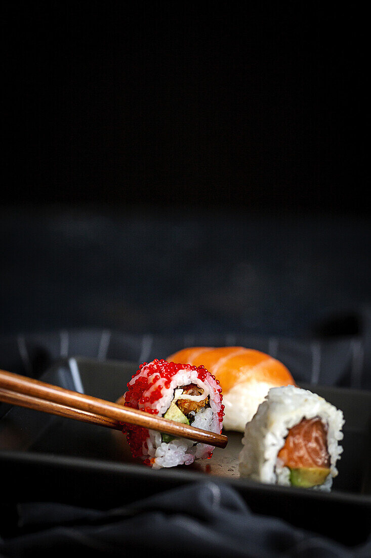 Top view Komposition von köstlichen frischen verschiedenen Sushi und Bambus-Essstäbchen auf schwarzem Teller auf karierten Tuch serviert