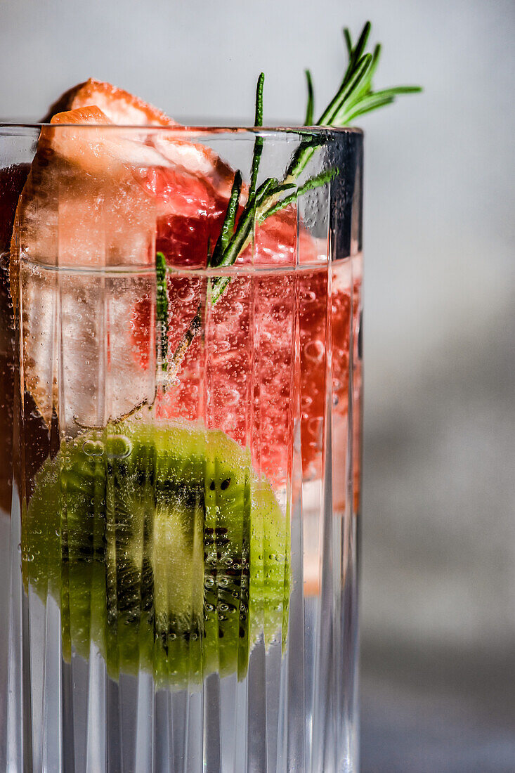 Tropischer Sommercocktail aus Wodka und Sprite mit reifen Früchten und Rosmarin auf grauem Hintergrund