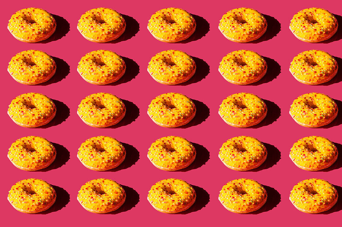 Top view of many donuts covered with yellow cover and colored balls on pink background