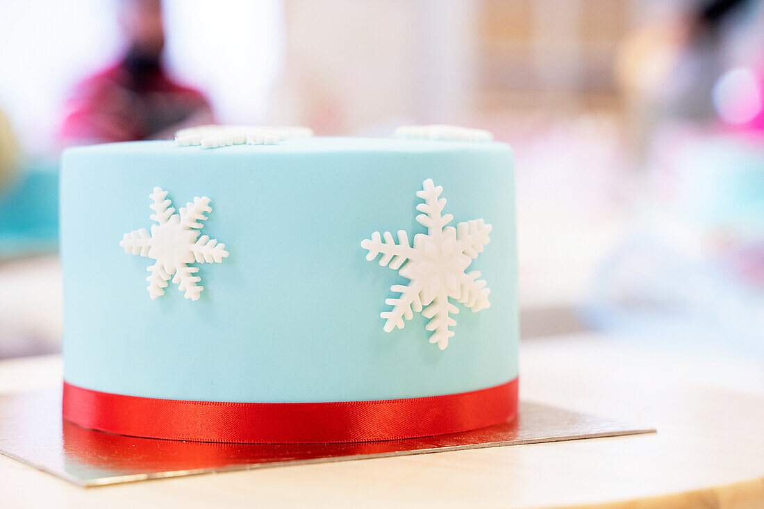 Decorated festive cake with white edible snowflakes and blue glaze on golden stand