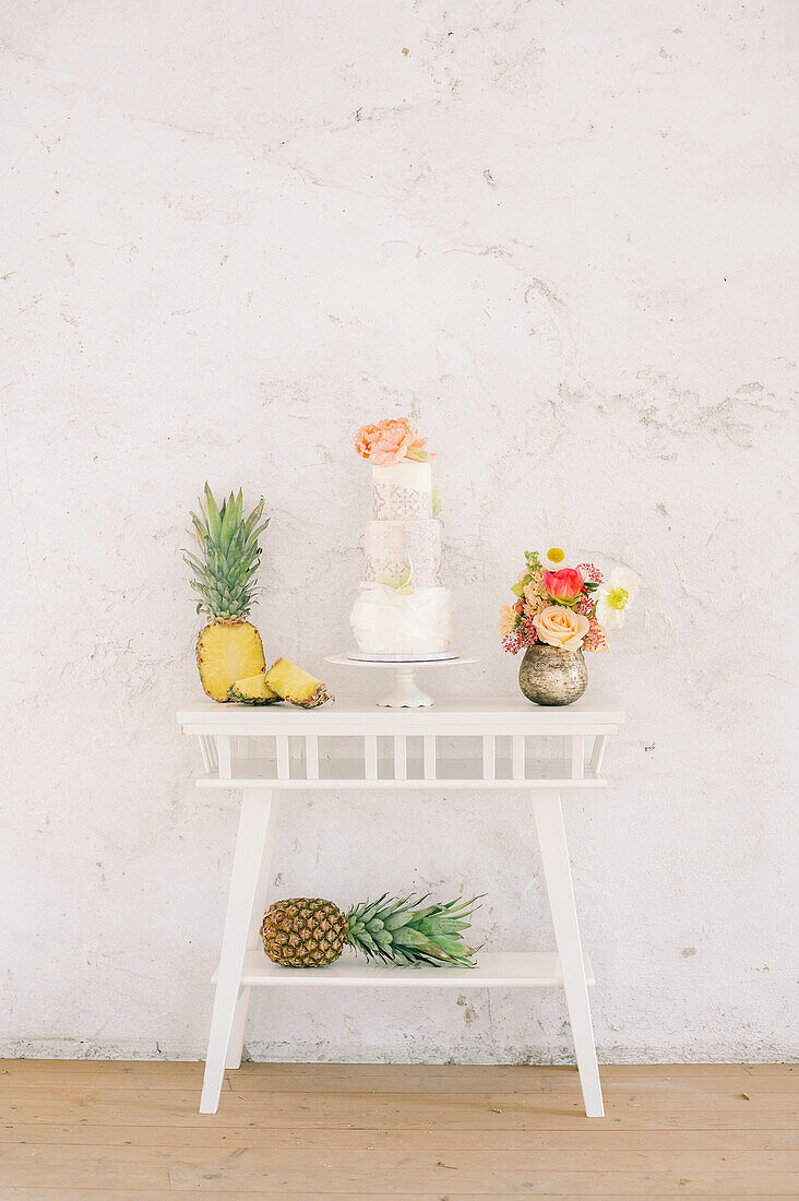 Frische Ananas und leckerer Kuchen auf dem Tisch neben roten hochhackigen Schuhen an einer weißen Wand während einer Hochzeitsfeier