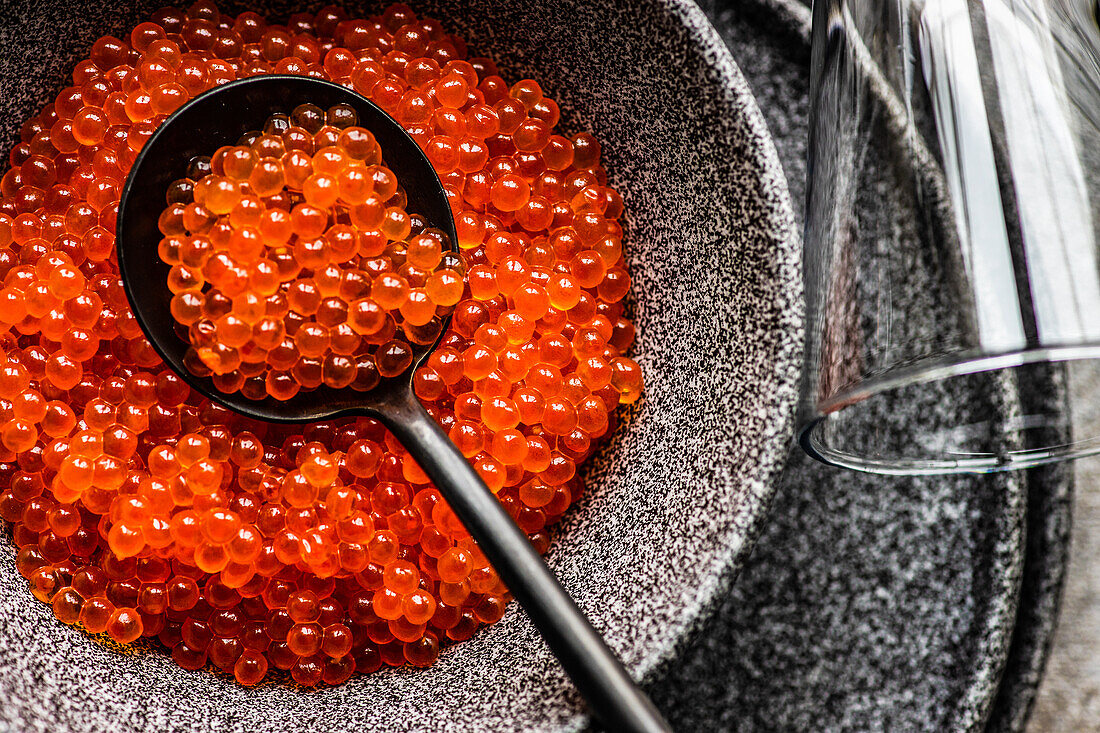 From above red fresh trout fish caviar served in a bowl on concrete table background