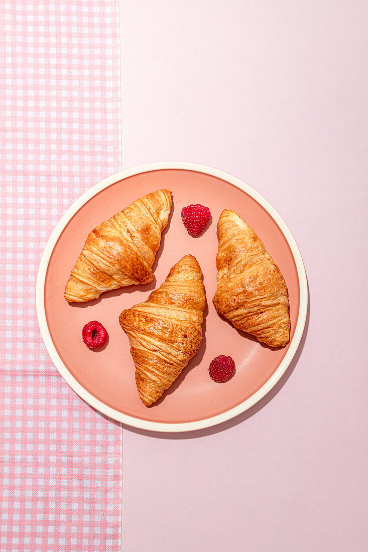 From above of composition of plated with fresh baked sweet croissants served with berries placed on pink table