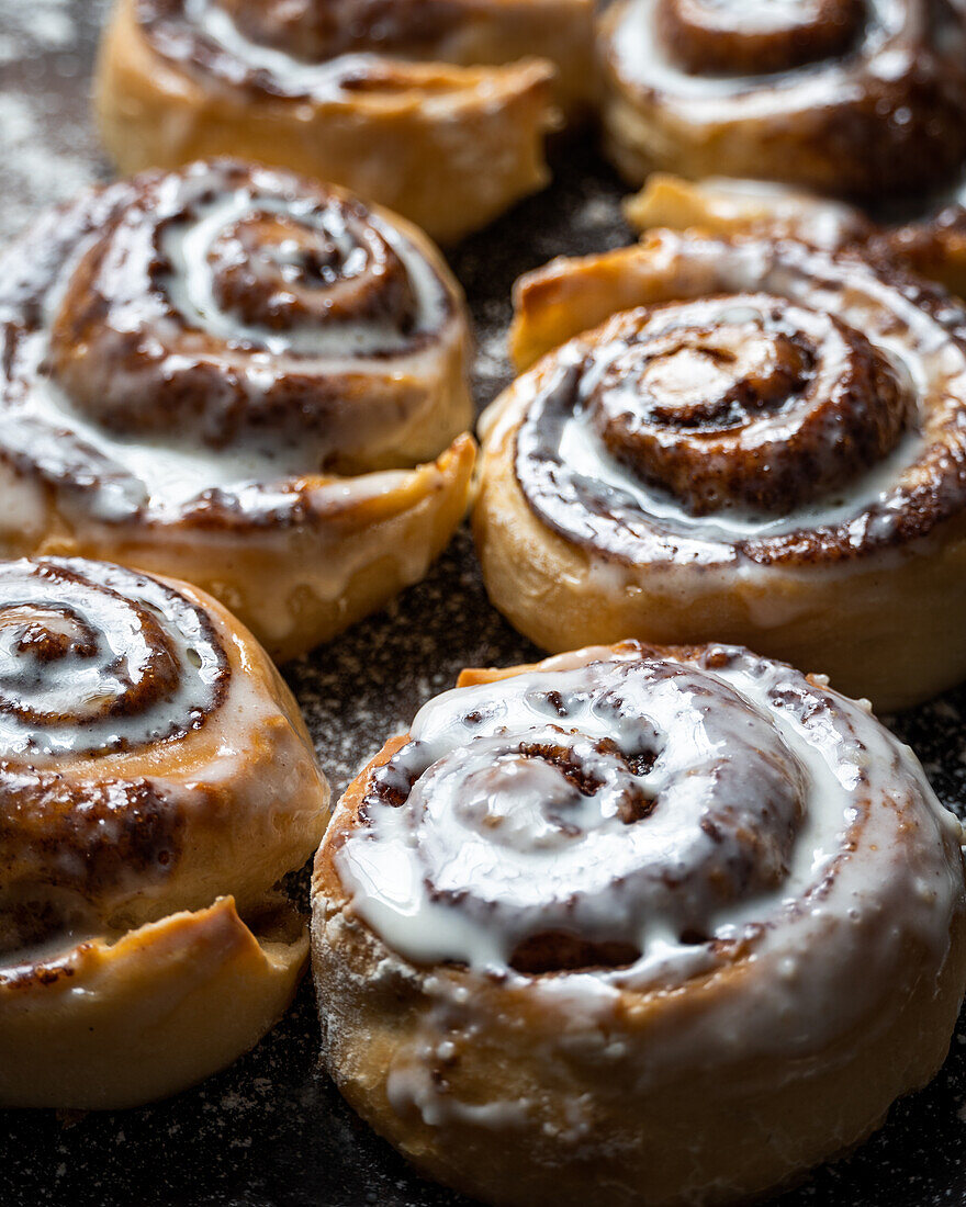 Appetizing baked sweet cinnamon rolls with white cream topping served on table in bakery