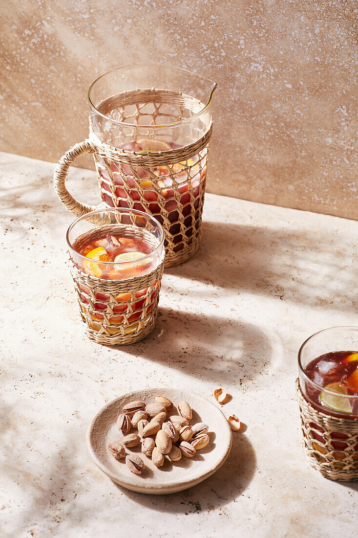 Blick von oben auf ein mit Sangria-Cocktail und Zitrusfrüchten gefülltes Glasgefäß, das an einem warmen Sommertag auf einem Keramiktisch neben Nüssen steht