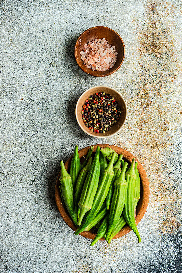 From above preparation for cooking of bamia vegetable with pepper and himalayan salt on concrete background