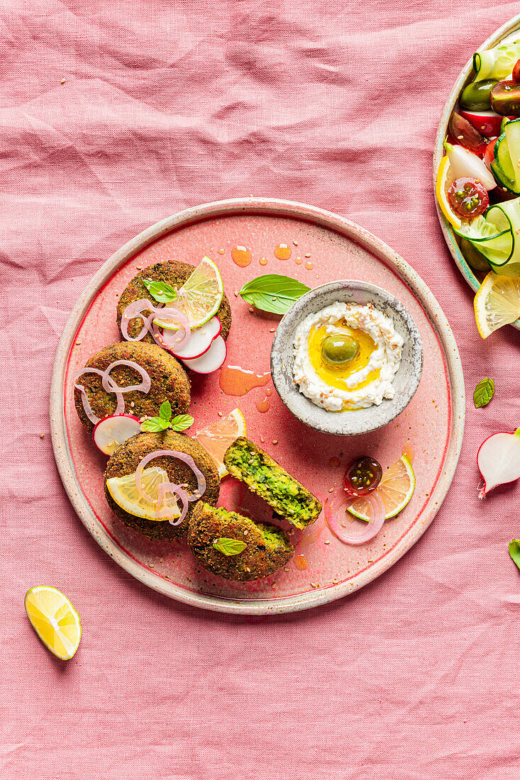 Top view of plate with delicious cream cheese and assorted vegetables placed on napkin near vegan fritters on pink background