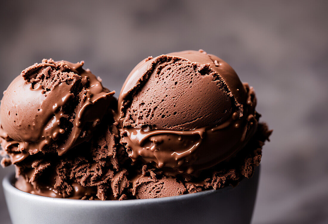 Tasty sweet chocolate ice cream scoops placed in white ceramic bowl against blurred gray background