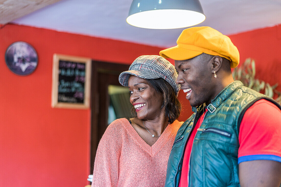 Seitenansicht eines positiven afroamerikanischen Paares in farbenfroher Kleidung, das in einer Bar steht und das Wochenende genießt