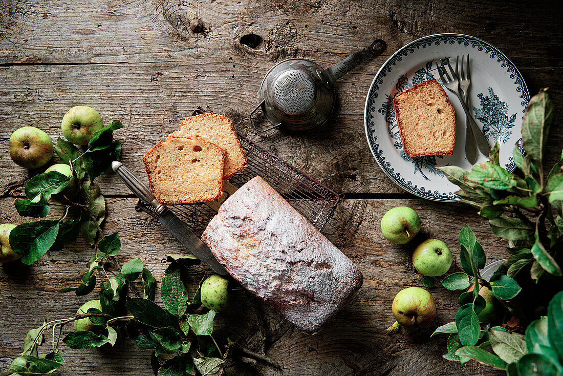 Draufsicht auf köstliches hausgemachtes Kuchenbrot mit Puderzucker auf einem Holztisch in der Nähe von frischen reifen Äpfeln