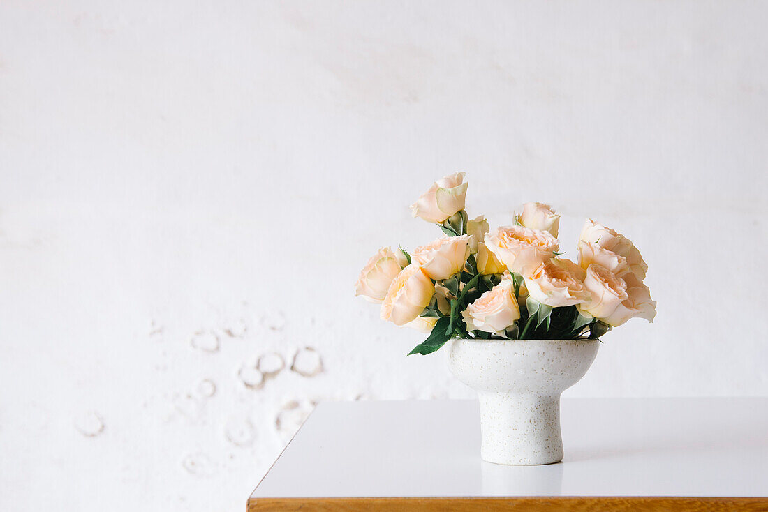 Blühende, duftende gelbe Rosen in einer Keramikvase auf einem Tisch in einer Blumenwerkstatt vor einer weißen Wand