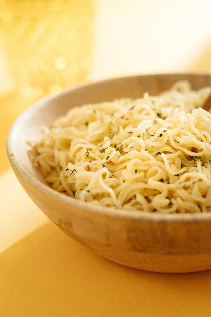 Close-up of bowl of delicious noodles with seasoning placed on yellow background with wooden chopsticks in light room