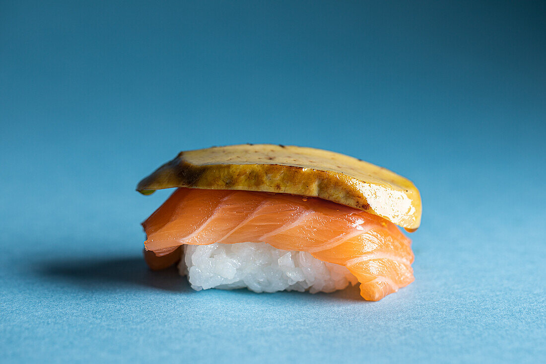 Traditionelle japanische Delikatessen Norwegische Nigiri mit frischem Lachs und schmackhafter flambierter Gänsestopfleber, serviert vor blauem Hintergrund in einem hellen Studio