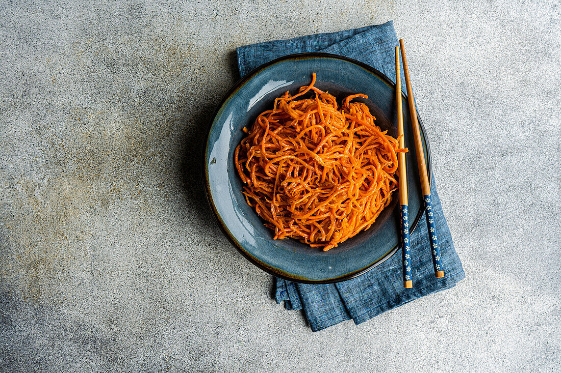 From above traditional spicy asian carrot salad served on ceramic plate and chopsticks on concrete background