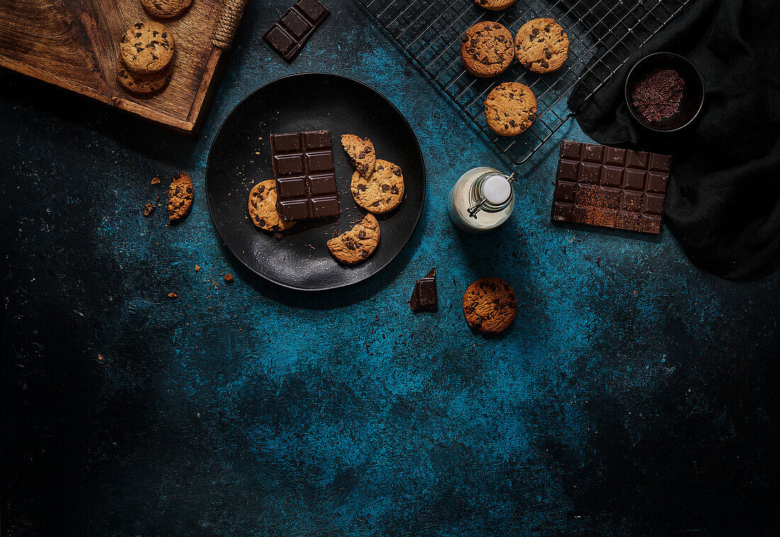 Top view of glass of fresh milk placed on dark blue table near yummy biscuits and chocolate bars