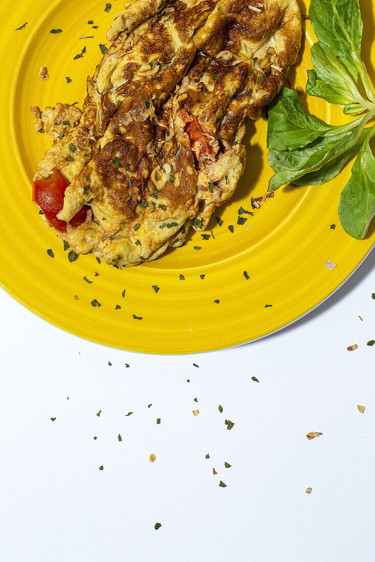 Delicious omelette with chopped parsley on plate against sun dried tomatoes on white background